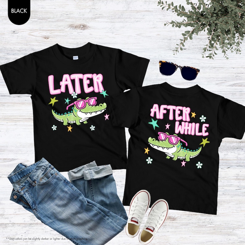 May include: Two black t-shirts with alligator graphics wearing sunglasses and the phrases "LATER" and "AFTER WHILE" in pink. The shirts are paired with blue jeans and white sneakers.
