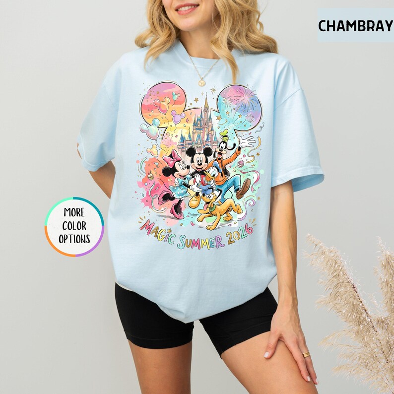 K&ouml;nnte beinhalten: Hellblaues T-Shirt mit einem farbenfrohen Aufdruck von Mickey Mouse, Minnie Mouse, Donald Duck, Goofy und Pluto vor einem Schloss. Der Text "Magic Summer 2026" ist ebenfalls auf dem Shirt zu sehen. Das Shirt hat kurze &Auml;rmel.