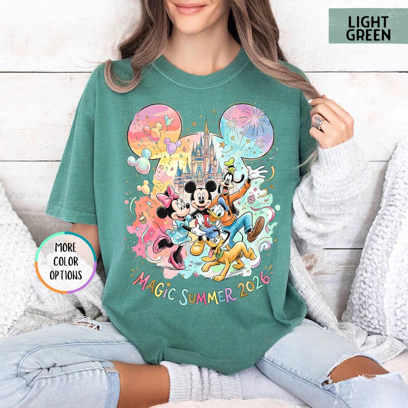 K&ouml;nnte beinhalten: Hellgr&uuml;nes T-Shirt mit einem farbenfrohen Disney-Motiv, das Micky Maus, Minnie Maus, Donald Duck, Goofy und Pluto zeigt. Das Design beinhaltet ein Schloss, Feuerwerk und den Text "Magic Summer 2026".
