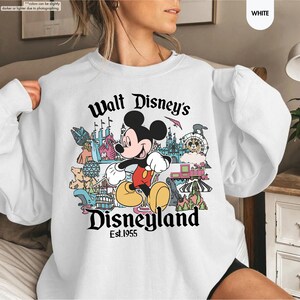 Pu&ograve; includere: Felpa bianca con una grafica colorata di Topolino e delle attrazioni di Disneyland. Il testo "Walt Disney's Disneyland Est.1955" &egrave; stampato in nero. La felpa &egrave; a girocollo.