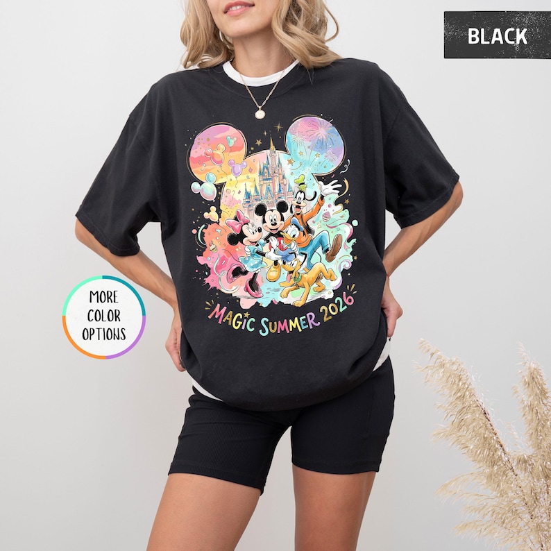 K&ouml;nnte beinhalten: Schwarzes T-Shirt mit einem farbenfrohen Aufdruck von Mickey Mouse, Minnie Mouse, Donald Duck, Goofy und Pluto vor einem Schloss. Der Text "Magic Summer 2026" ist darunter gedruckt. Das T-Shirt hat einen Rundhalsausschnitt und kurze &Auml;rmel.