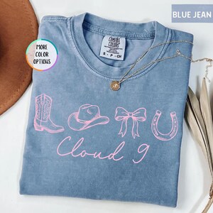 May include: A white ceramic mug with a black handle and the text "But First, Coffee" in a bold, black font. The mug is set against a blurred background, suggesting a cozy setting.