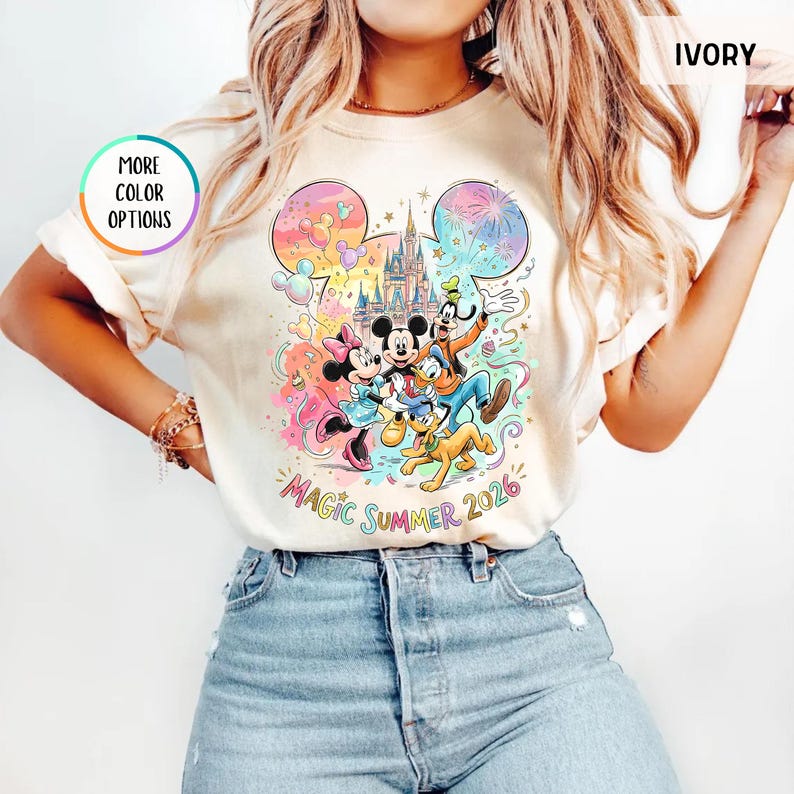 K&ouml;nnte beinhalten: Elfenbeinfarbenes T-Shirt mit einem farbenfrohen Aufdruck von Mickey Mouse, Minnie Mouse, Donald Duck, Goofy und Pluto vor einem Schloss. Der Text "Magic Summer 2026" ist darunter. Das Shirt hat einen Rundhalsausschnitt und kurze &Auml;rmel.