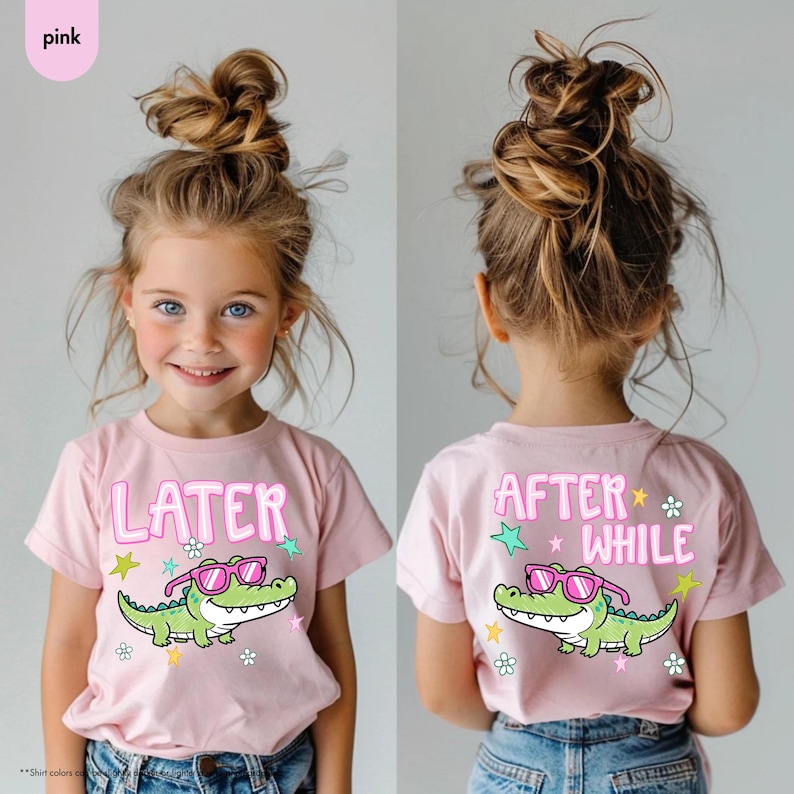 May include: Pink short-sleeved t-shirt with a cartoon alligator wearing sunglasses. The front of the shirt says "LATER" and the back says "AFTER WHILE". The shirt has a crew neck and is worn by a young child.