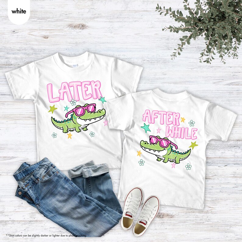 May include: Two white t-shirts with a cartoon alligator wearing pink sunglasses. One shirt says "LATER" and the other says "AFTER WHILE" in pink bubble letters. Blue jeans and white sneakers are also in the image.