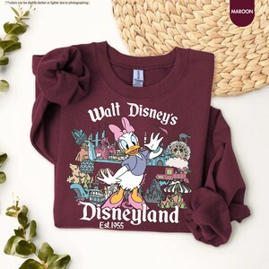Pu&ograve; includere: Felpa bordeaux con una grafica di Paperina davanti alle attrazioni di Disneyland. Il testo "Walt Disney's Disneyland Est.1955" &egrave; stampato in bianco. La felpa &egrave; realizzata in materiale morbido e ha maniche lunghe.
