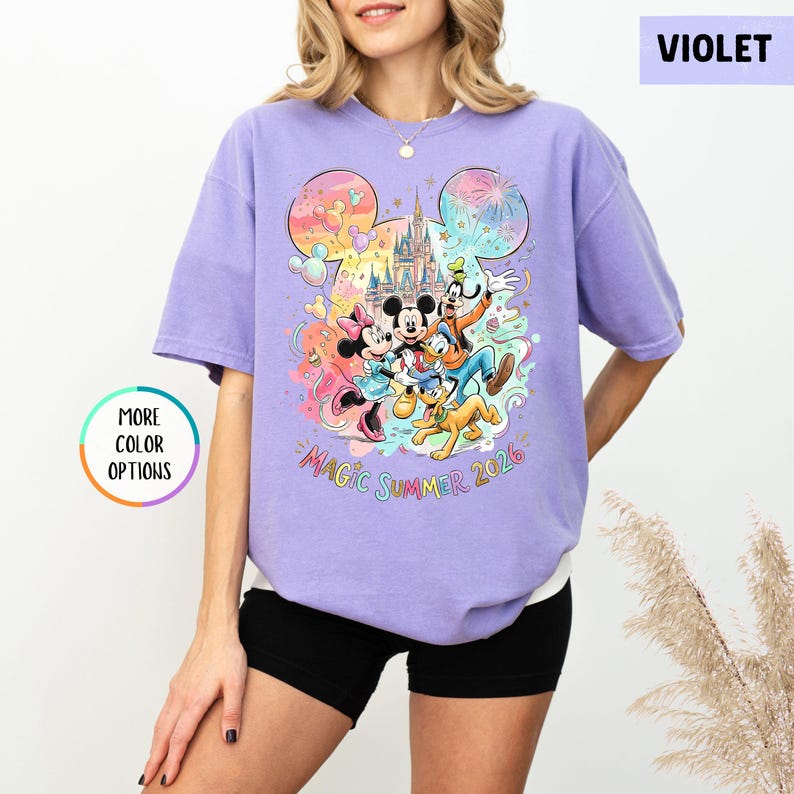 K&ouml;nnte beinhalten: Ein violettes T-Shirt mit einem farbenfrohen Aufdruck von Disney-Figuren, darunter Micky und Minnie Maus, Donald Duck und Goofy, vor einem Schloss. Der Text "MAGIC SUMMER 2026" ist darunter. Das Shirt hat eine lockere Passform.