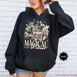 以下が含まれることがあります： お城、ミッキーマウスの耳、そして「The Most Magical Place」の文字が描かれた、カラフルなグラフィックが特徴の黒いフード付きスウェットシャツ。デザインにはピンク、イエロー、ホワイトのアクセントが含まれています。