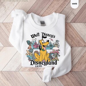 Pu&ograve; includere: Felpa bianca con grafica colorata di Disneyland con Pluto. Il design include il testo "Walt Disney's Disneyland Est. 1955". La felpa &egrave; realizzata in materiale morbido.