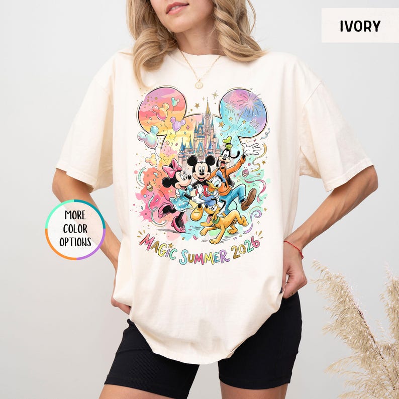 K&ouml;nnte beinhalten: Elfenbeinfarbenes T-Shirt mit einer farbenfrohen Grafik von Mickey Mouse, Minnie Mouse, Donald Duck, Goofy und Pluto vor einem Schloss. Der Text "Magic Summer 2026" steht darunter. Das Shirt hat kurze &Auml;rmel.