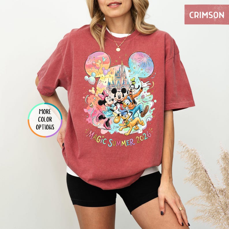 K&ouml;nnte beinhalten: Karmesinrotes T-Shirt mit einem farbenfrohen Aufdruck von Mickey Mouse, Minnie Mouse, Donald Duck, Goofy und Pluto vor einem Schloss. Der Text "Magic Summer 2026" steht darunter. Das T-Shirt hat kurze &Auml;rmel.
