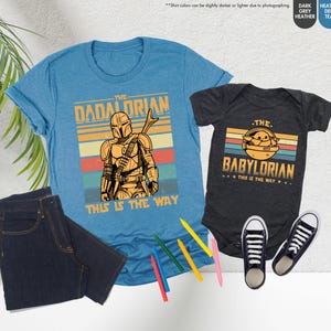 以下が含まれることがあります： スターウォーズをテーマにしたグラフィックが特徴の、水色のTシャツと濃いグレーのベビーボディスーツ。Tシャツには「The Dadalorian」、ボディスーツには「The Babylorian」と書かれています。どちらも「This is the Way」というフレーズが入ったレトロなデザインです。
