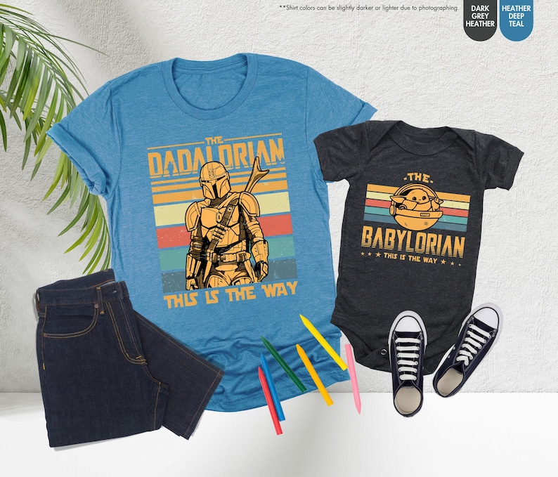 以下が含まれることがあります： スターウォーズをテーマにしたグラフィックが特徴の、水色のTシャツと濃いグレーのベビーボディスーツ。Tシャツには「The Dadalorian」、ボディスーツには「The Babylorian」と書かれています。どちらも「This is the Way」というフレーズが入ったレトロなデザインです。