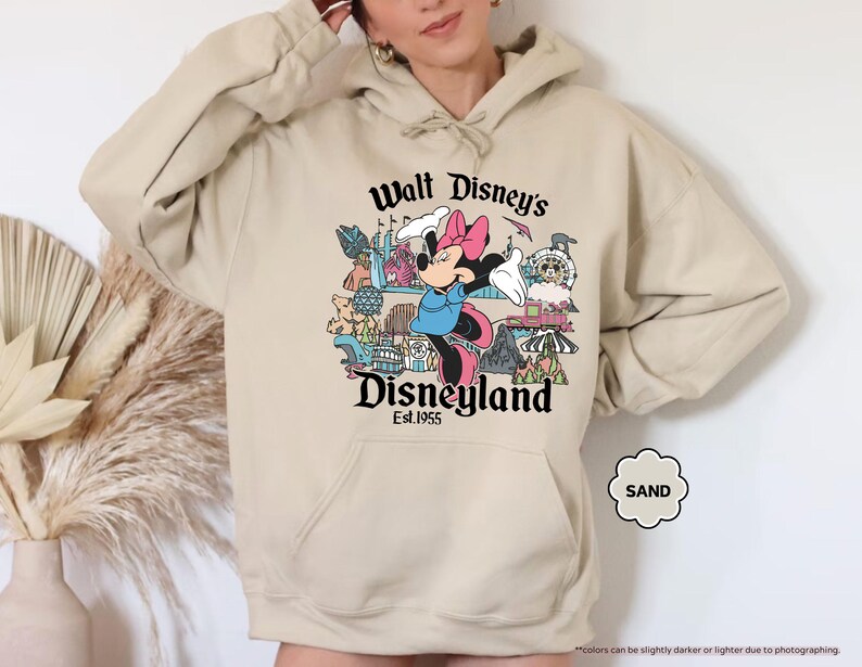 Pu&ograve; includere: Felpa con cappuccio color sabbia con una grafica di Minnie Mouse davanti a Disneyland. Il testo "Walt Disney's Disneyland Est. 1955" &egrave; stampato sopra e sotto l'immagine. La felpa ha una tasca a marsupio e un cappuccio con coulisse.