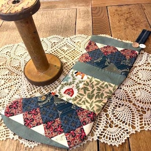 May include: A handmade Christmas stocking with a patchwork design. The stocking features various fabric patterns, including floral, geometric, and patterned prints in shades of blue, red, and green. It has a denim loop with a button closure.