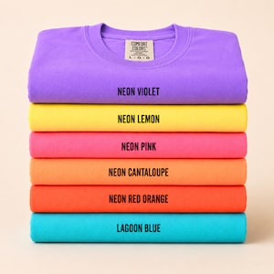 May include: A stack of six Comfort Colors crewneck sweatshirts in vibrant neon colors: Neon Violet, Neon Lemon, Neon Pink, Neon Cantaloupe, Neon Red Orange, and Lagoon Blue. Each shirt displays its color name in black text.