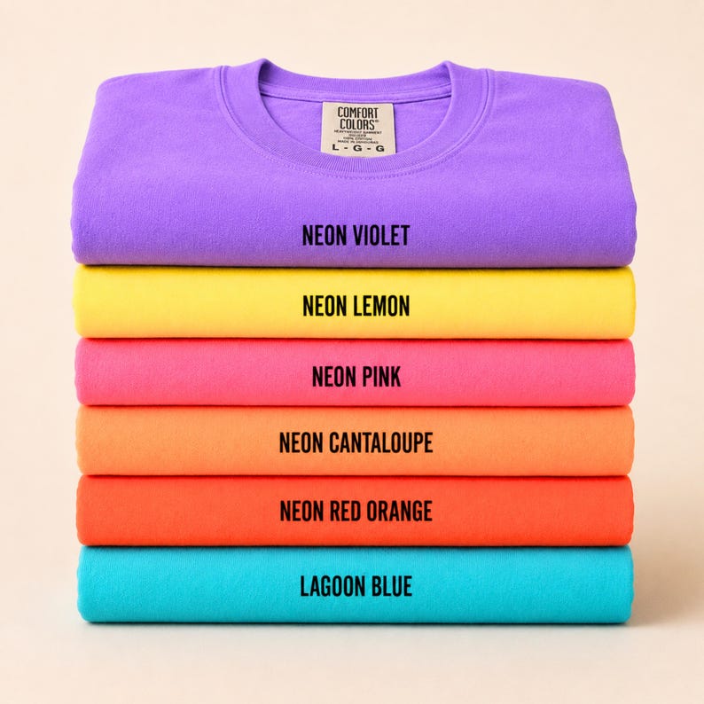 May include: A stack of six Comfort Colors crewneck sweatshirts in vibrant neon colors: Neon Violet, Neon Lemon, Neon Pink, Neon Cantaloupe, Neon Red Orange, and Lagoon Blue. Each shirt displays its color name in black text.