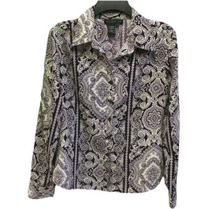 Puede incluir: Una camisa abotonada de manga larga con un estampado de cachemira en tonos morado, negro y blanco. La camisa tiene cuello y está colgada de una percha negra. La tela presenta un diseño intrincado y repetitivo.