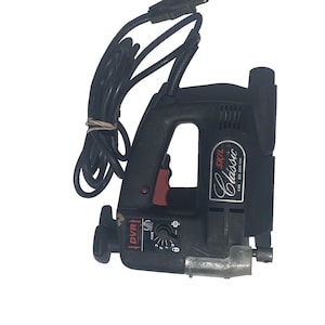 May include: Black Skil Classic jigsaw with a black power cord. The tool has a red trigger and a dial with numbers. The text "DVR" is visible on the side. The tool is designed for cutting wood and other materials.