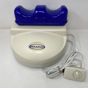 Könnte beinhalten: Ein weiß-blauer Relaxus-Massagegerät. Das Massagegerät hat eine geschwungene blaue Oberseite und eine weiße Basis mit dem Aufdruck "RELAXUS". Es enthält ein weißes Netzkabel und einen Drehregler.