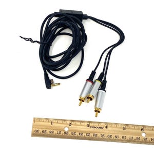 May include: Black audio/video cable with a 3.5mm jack and three RCA connectors. The RCA connectors have red, yellow, and white bands. A wooden ruler is in the foreground, with measurements in inches.
