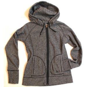 May include: A gray hooded sweatshirt with a full-length black zipper and two front pockets. The sweatshirt has a drawstring hood and thumb holes at the cuffs. The brand logo is visible on the lower right side.