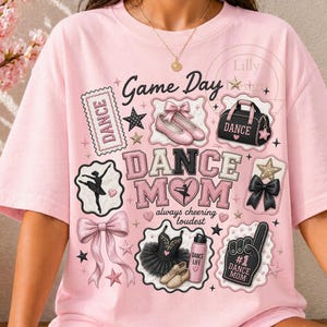 Pode incluir: Camiseta rosa claro com um design temático de dança. O design inclui as palavras "Game Day" e "Dance Mom", sapatilhas de ballet, estrelas, laços e uma silhueta de bailarina. A frase "always cheering loudest" também está incluída.