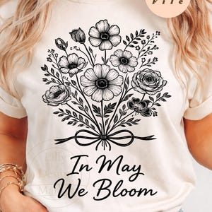Puede incluir: Camiseta color crema con un diseño de ramo floral negro y el texto "In May We Bloom". El ramo incluye varios tipos de flores y follaje atados con un lazo. El diseño es un archivo PNG.