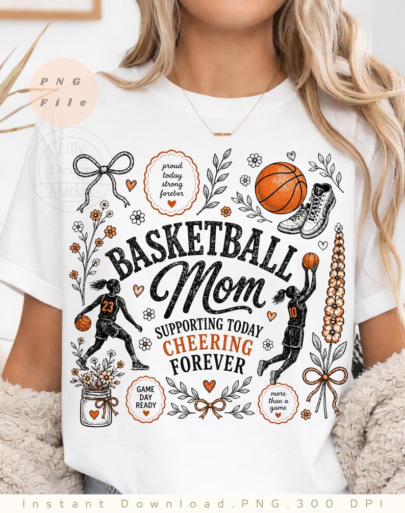 Puede incluir: Camiseta blanca con un dise&ntilde;o tem&aacute;tico de baloncesto. El dise&ntilde;o incluye las palabras "Basketball Mom" con texto de apoyo, ilustraciones de baloncesto y detalles florales. La camiseta tiene cuello redondo y mangas cortas.