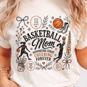 Puede incluir: Camiseta de color crema con un gr&aacute;fico tem&aacute;tico de baloncesto. El dise&ntilde;o incluye las palabras "Basketball Mom" con texto de apoyo e ilustraciones de baloncesto. La camiseta presenta una pelota de baloncesto, zapatillas y detalles florales.
