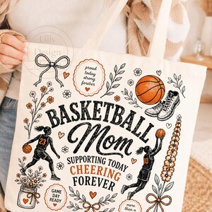 Puede incluir: Bolso tote de color crema con tem&aacute;tica de baloncesto. El dise&ntilde;o incluye las palabras "Basketball Mom" y "Supporting Today Cheering Forever". Presenta ilustraciones de una pelota de baloncesto, una zapatilla de ca&ntilde;a alta y jugadores de baloncesto. Acentos florales y de coraz&oacute;n completan el dise&ntilde;o.