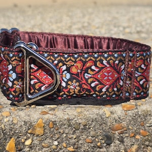 Könnte beinhalten: Ein dekoratives Hundehalsband mit einem Muster in Rot, Orange, Blau und Weiß auf schwarzem Hintergrund. Das Halsband hat ein bordeauxfarbenes Satinfutter und eine silberfarbene Metallschnalle.