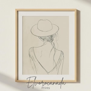Può includere: Stampa artistica incorniciata con un disegno a tratto minimalista di una persona con un cappello, vista da dietro. L'opera d'arte è in bianco e nero su sfondo beige, incorniciata in legno chiaro. La stampa è firmata "Elvorocanada Prints".