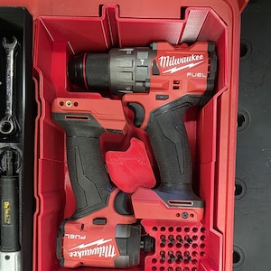 May include: Red Milwaukee FUEL power tools, including a drill and impact driver, are stored in a red tool case. The case has custom compartments for secure storage and easy access. The tools have black grips.