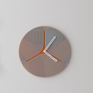 Peut inclure: Une horloge murale ronde et moderne au design unique. Le cadran présente un motif de lignes marron et blanches, avec un centre orange et des aiguilles blanches. L'horloge mesure environ 30 cm de diamètre.