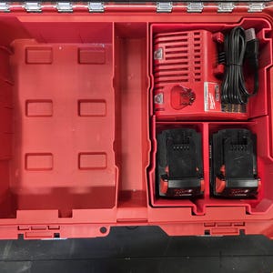 May include: A red plastic tool case with several compartments. Inside, there's a red battery charger, two black batteries, and empty storage areas. The case is open, displaying its contents.