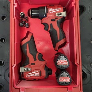 Può includere: Un kit di utensili elettrici Milwaukee rosso con un trapano, un avvitatore a impulsi e due batterie. Gli utensili sono neri e rossi e il kit include varie punte per trapano. Il kit è riposto in una valigetta rossa.