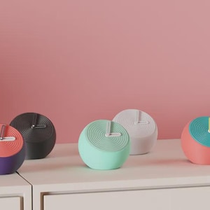 Puede incluir: Una colección de relojes esféricos modernos en varios colores, incluyendo morado, negro, verde menta, blanco y coral. Cada reloj presenta un diseño espiral único en la esfera y un color contrastante en la sección superior.