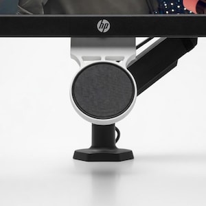 May include: A computer monitor with a black frame and the HP logo. The monitor is mounted on a white and black stand with a circular speaker. The stand is on a white surface.
