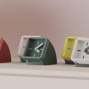 Può includere: Una collezione di sveglie moderne e colorate. Ogni orologio ha un quadrante quadrato con una combinazione di colori contrastanti, tra cui arancione, verde, giallo e bianco. Gli orologi sono esposti su una superficie bianca su uno sfondo rosa tenue.