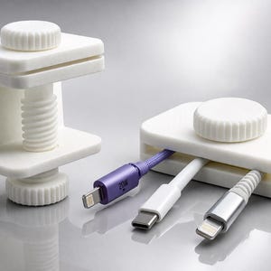 Peut inclure: Organisateurs de câbles blancs avec des boutons à visser et des fentes pour les câbles. L'un est une pince, l'autre est une boîte rectangulaire. Trois câbles, violets, blancs et argentés, sont branchés dans la boîte.