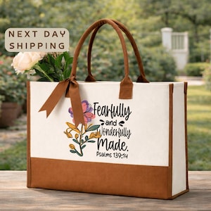 May include: A canvas tote bag with brown handles and a brown bottom panel. The bag features the text "Fearfully and Wonderfully Made" with floral accents. A bouquet of flowers and a ribbon are visible.