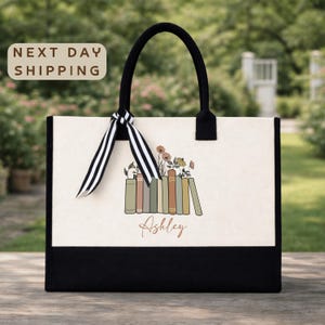 A tote bag with a floral design and the name "Ashley" printed on it, placed on a wooden surface with a garden in the background.