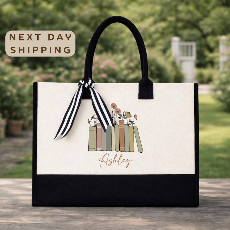 A tote bag with a floral design and the name "Ashley" printed on it, placed on a wooden surface with a garden in the background.