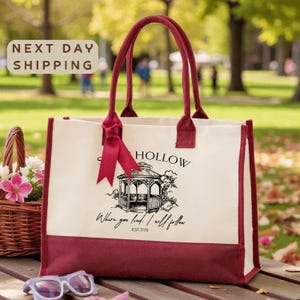 A red and white tote bag with a graphic design and text, placed on a wooden surface with a basket of flowers and sunglasses nearby.