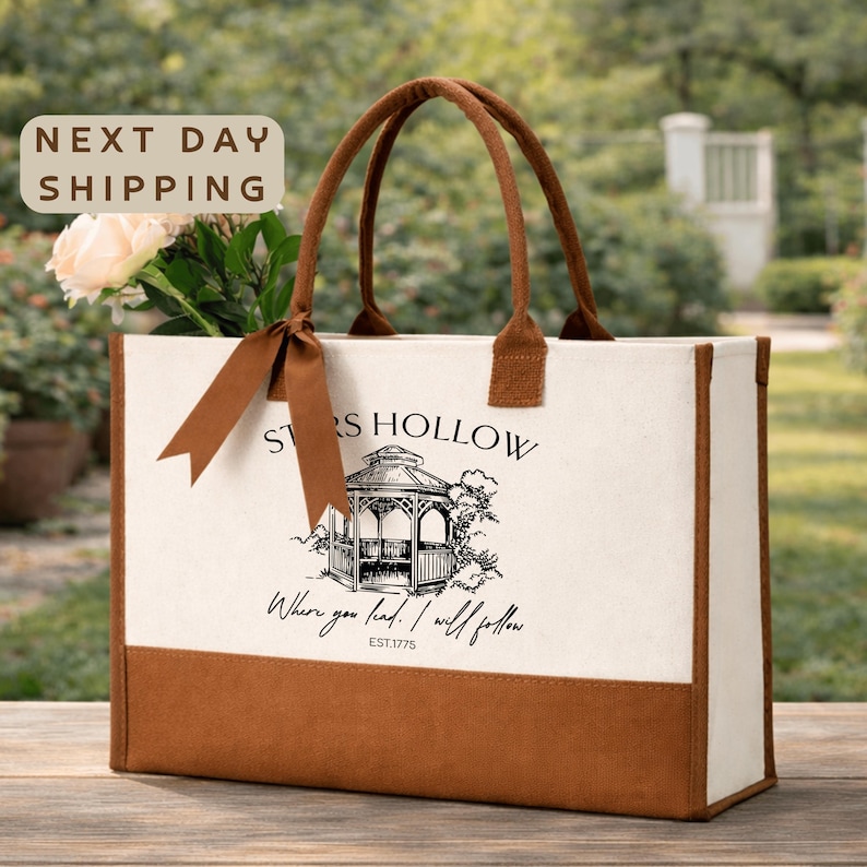 a beige tote bag with a printed design of a gazebo and the text "Stores Hollow" printed on it. The bag is placed on a wooden surface, and there is a sign that says "Next day shipping".