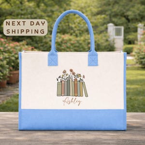 A blue and white tote bag with a floral design and the name "Ashley" printed on it, placed on a wooden surface.