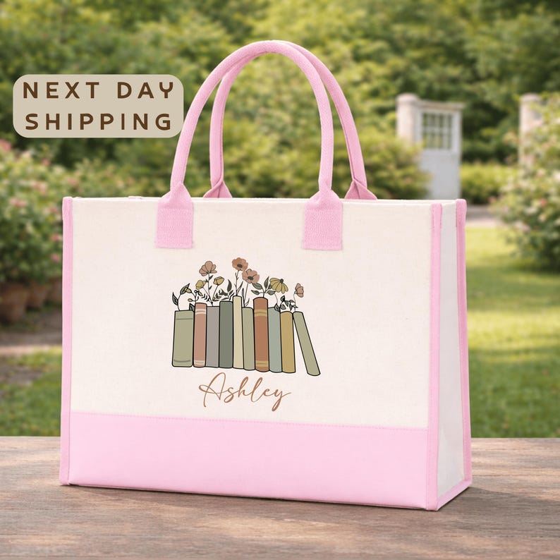 A pink tote bag with a floral design and the name "Ashley" printed on it, placed on a wooden surface.