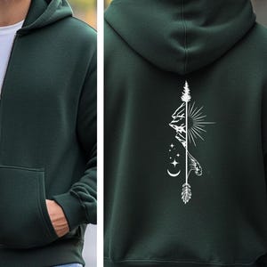 May include: Dark green zip-up hoodie with a white graphic on the back featuring a mountain range, sun, stars, and an arrow. The hoodie has a hood, a front pocket, and a white zipper.