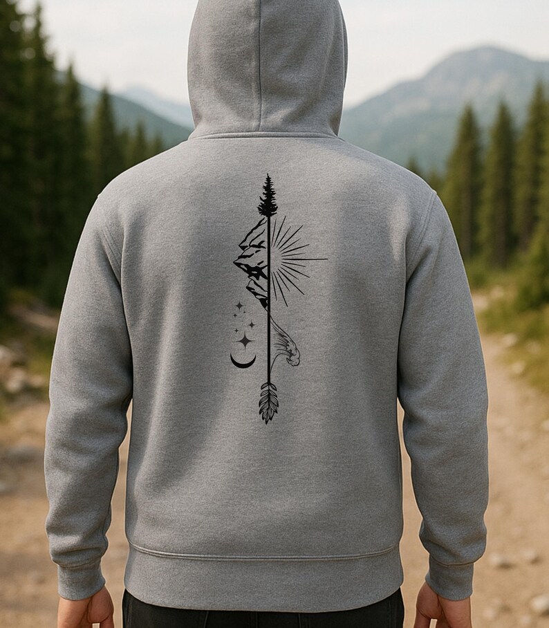 May include: A gray hooded sweatshirt with a black graphic design on the back. The design features a mountain, sun, stars, moon, and feather. The sweatshirt has a drawstring hood and long sleeves. The background shows a forest and mountains.